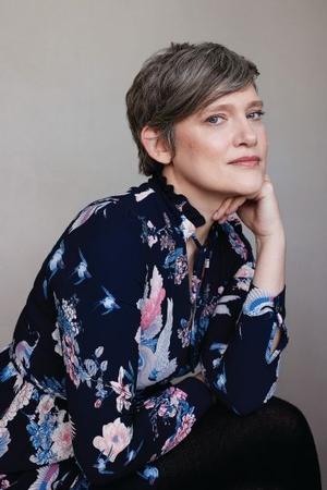 Portrait photo of Heather O'Neill, seated and leaning forward with chin on hand