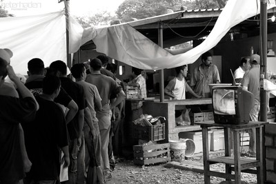 Black and white photo showing a line of migrants outside a tented area
