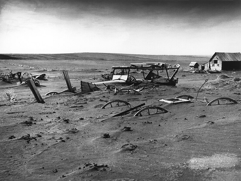 Farm machinery buried in dust outside a barn, taken in Dallas, South Dakota, 1936