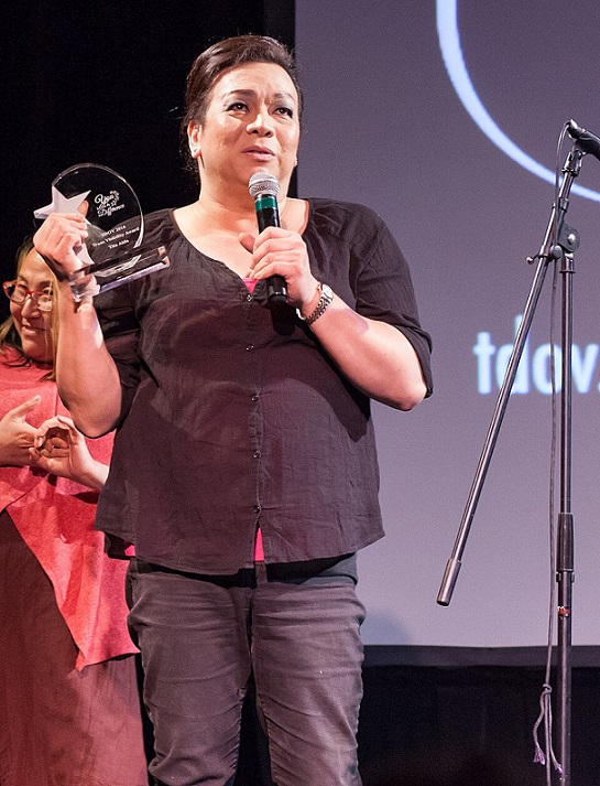 Nicky Calma aka Tita Aida holding a microphone and an etched glass award